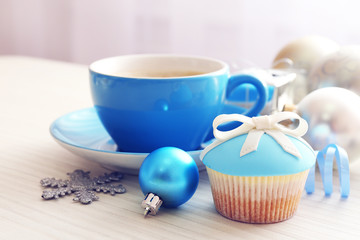 Tasty cupcake with bow, coffee cup and Christmas toys on color wooden background