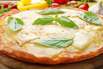 Tasty pizza decorated with basil and vegetables on wooden background, close up
