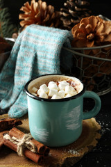 Mug of hot cacao with marshmallow and gloves on black table