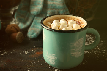 Mug of hot cacao with marshmallow and gloves on black table