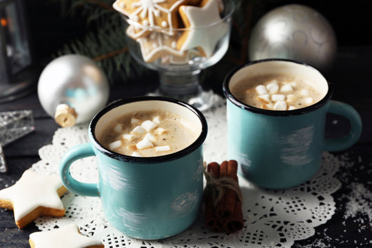 Two mugs of hot cacao with marshmallow and cookies on black table
