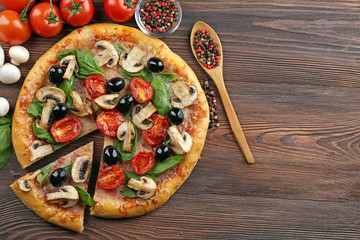 Sliced delicious tasty pizza with vegetables on wooden table