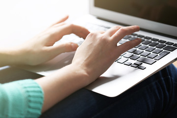 Woman sitting on sofa with a laptop on her knees in a room