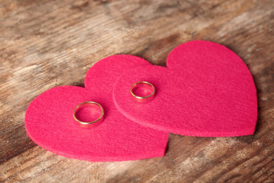 Two red felt hearts and wedding rings on wooden background closeup