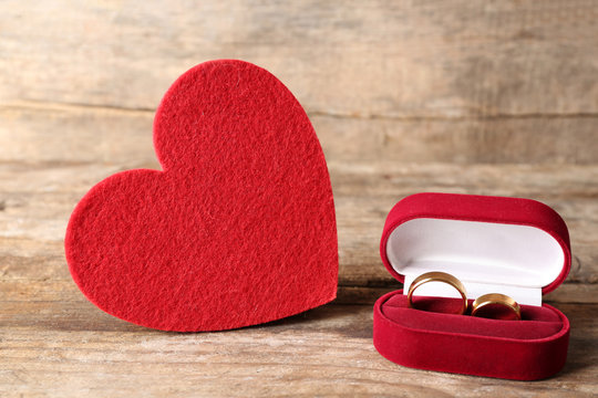 Red velvet silk heart and wedding rings in a box on wooden background closeup