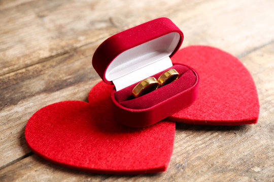 Two red hearts and wedding rings in velvet silk box on wooden background closeup