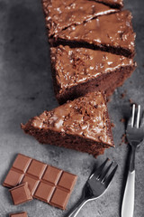 Tasty sliced cake with chocolate and forks on grey background, close up