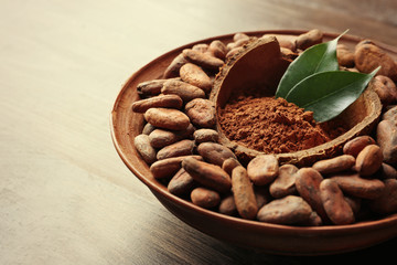 Bowl with aromatic cocoa harvest on wooden background, close up