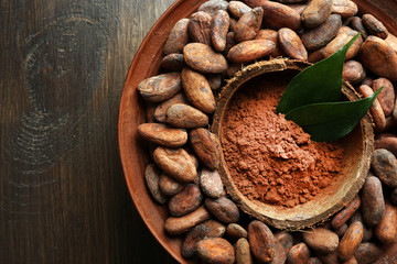 Bowl with aromatic cocoa harvest on wooden background, close up