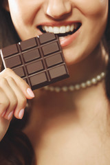 Loving chocolate woman bites bar to enjoy the taste, close up