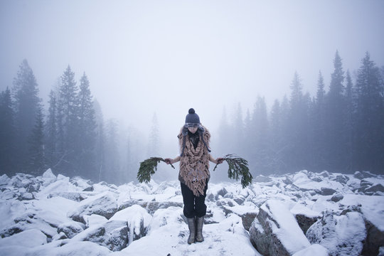 Woman holding tree branches on snow covered rocks