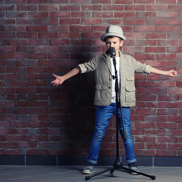 Little boy singing with microphone on a brick wall background