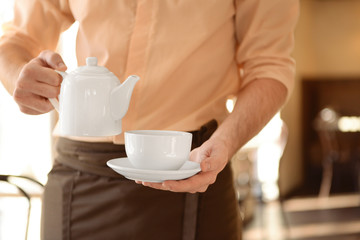 Waiter holding teapot and cup close up