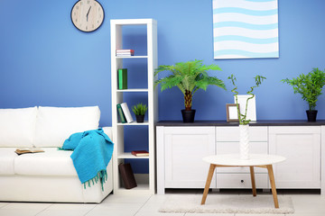Room interior with commode, bookcase, table and sofa on blue wall background