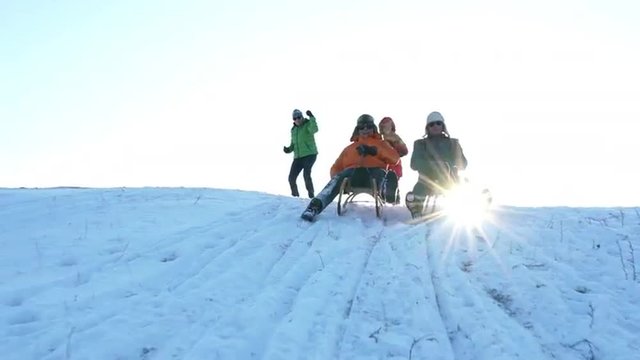 happy best ager couples enjoying sunny winter day outdoors on snowy hill, wives pushing and cheering their tobogganing laughing husbands

