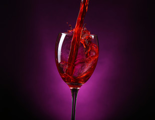 Wine pouring in glass on dark purple background