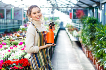 Beautiful happy young woman gardener holding water sprayer in greenhouse