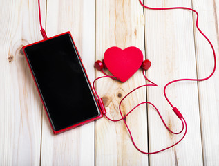 Red Smart Phone With Blank Screen, Red Earphones And Little Red Heart On Wooden Desk. Love Concept.