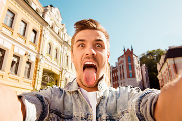 Funny happy man making comic selfie with tongue on the street