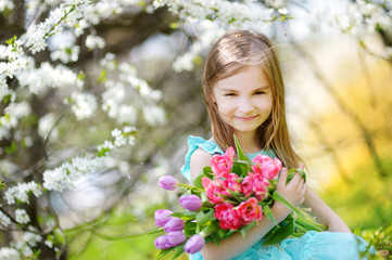 Naklejka premium Adorable little girl holding tulips for her mother in cherry garden