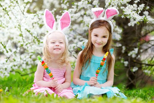 Two adorable little sisters eating colorful gum candies on Easter