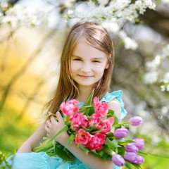 Adorable little girl holding tulips for her mother in cherry garden