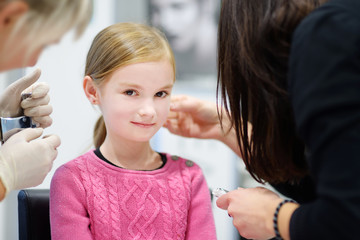 Adorable little girl having ear piercing process in beauty center - obrazy, fototapety, plakaty