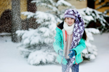 Happy adorable kid girl wearing a colorful jacket and knitted hat playing in a beautiful snowy winter park on beauty day
