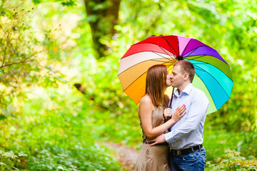 Пара влюбленных молодых людей прячется от дождя в лесу под зонтом 
