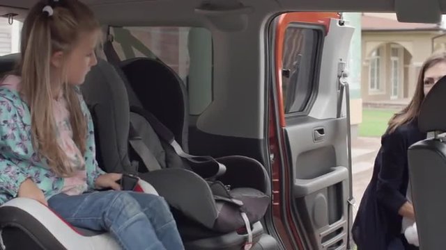 Young mother putting her little daughter in the baby car seat and fasten seat belts