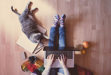 Creative workspace: girl working at the computer assisted by her cat.