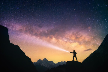 Silhouette of the man standing against the Milky Way in the mountains with a flashlight in his hands. Nepal, Everest region, view of the mount Thamserku (6,608 m) from Thame village (3,750 m). - obrazy, fototapety, plakaty