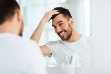 happy young man looking to mirror at home bathroom