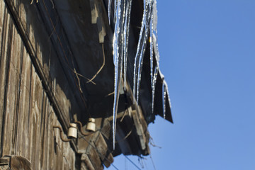 Icicles from the roof of a wooden house on a background of blue sky