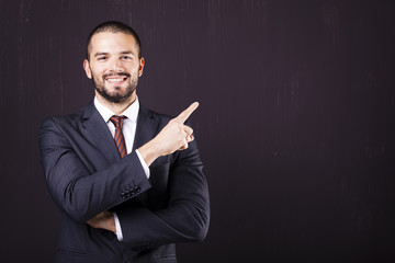 Smiling business man pointing at copy space against dark backgro