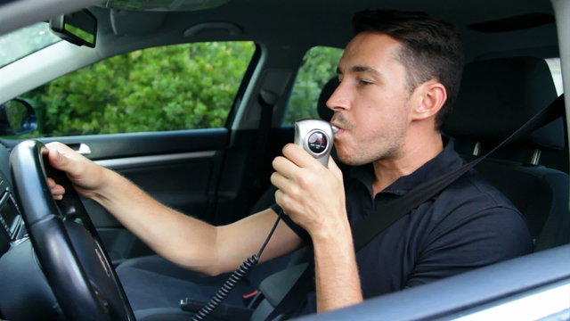 Young man blowing into alcohol breathalyser 