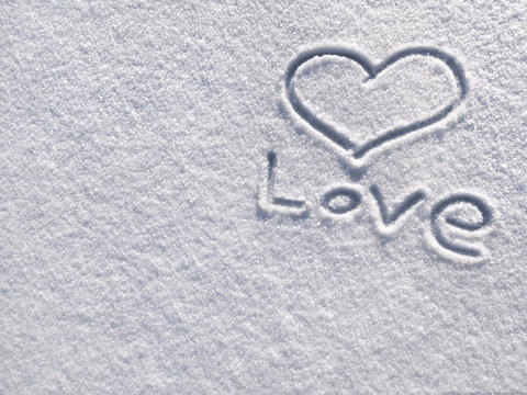 The symbol of the heart and word "love", painted on the fresh white snow. Love and St. Valentines Day concept.