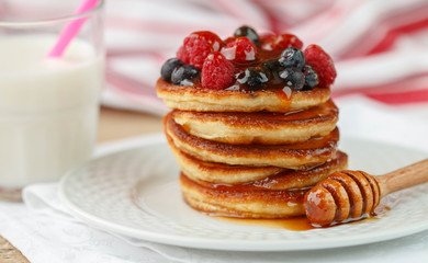 Breakfast. Fritters   with honey and berries - raspberries and blueberries on a white plate.  Homemade pancakes.  Selective focus
