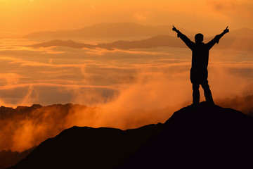Silhouette of tourist man spread hand on top of a mountain enjoy