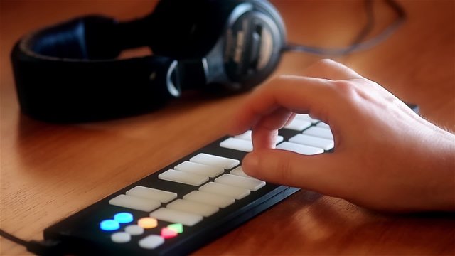 Playing on a MIDI keyboard with light up buttons and headphones laying aside defocused