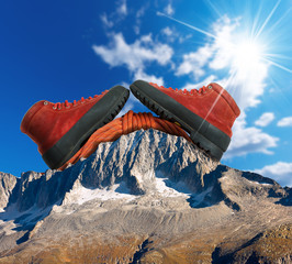 Mountain Climbing Concept / A pair of a mountaineering boots with a red climbing rope on a mountain peak with blue sky and sun rays.