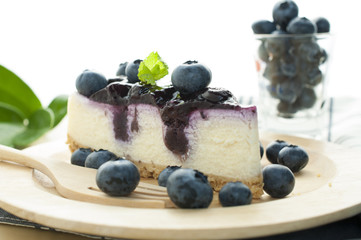 Blueberry cheesecake on wooden plate with plenty of blue berries
