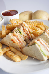 Club sandwiches with grilled chicken, tomato, lettuce, cheese, cucumber and dressing sauce, served on a white plate with french fries.