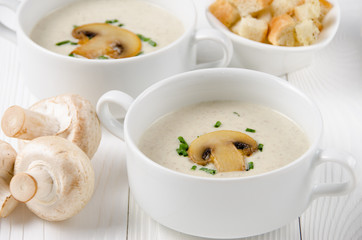 Mushroom cream soup in two white bowls with croutons and champig