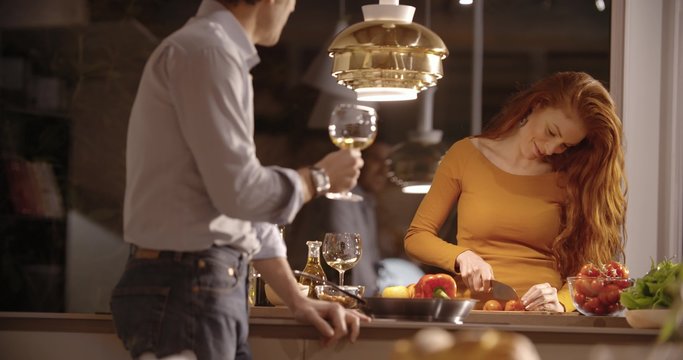 Woman cut raw vegetables for dinner while man drink wine at home in the evening in slow motion (in realtime at 60 fps)