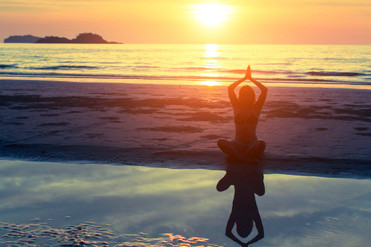 Woman silhouette practicing yoga on the beach at amazing sunset.