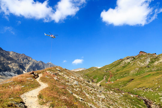 Transport helicopter flying with supplies and mountain panorama with alpine hut in Hohe Tauern Alps, Austria