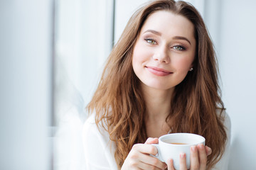 Smiling woman drinking coffe near the window