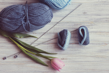 booties for newborns, spokes, two skeins of yarn, pink tulips lie on a blue background
