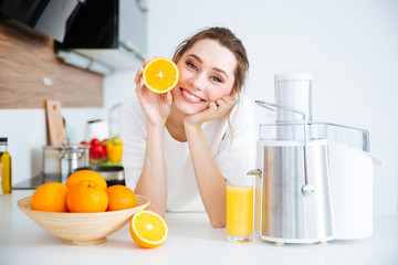 Cheerful woman showing half of orange sitting on kitchen